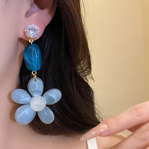 Close-up view of zircon and blue resin floral dangle earring worn by an Asian model