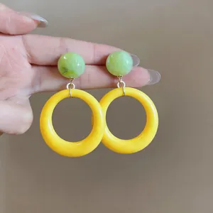 Detail shot of vibrant green marble-style resin and bright yellow hoop drop earrings.