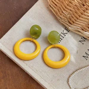 Detailed close-up of vibrant green resin beads and yellow circular hoop drop earrings.