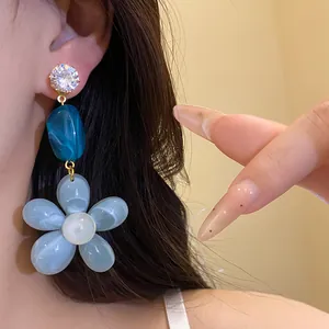 Close-up of blue resin flower pendant earrings with zircon stud for a summer vacation look.