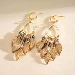 Detailed macro view of gold teardrop earrings with beads and leaf tassels in bohemian style.
