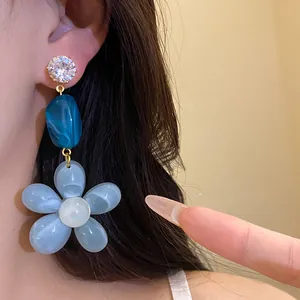 Detailed view of blue resin flower drop earrings with sparkling zircon stud on model's ear