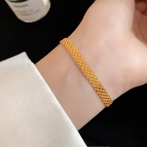 Close-up detail of a stylish gold-plated braided mesh chain bracelet on a wrist.