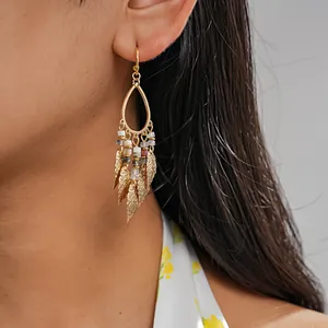 Close-up of gold-tone teardrop earrings with stone beads and leaf tassels on model