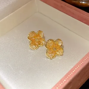 Detailed view of gold flower stud earrings with amber crushed stone inlay in a gift box