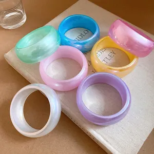 Gros plan de sept bracelets en résine colorée translucide posés sur un livre minimaliste