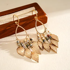 Close-up of golden teardrop earrings with multi-colored beads and metal leaf tassels.