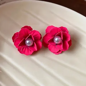 Elegant matte red flower stud earrings with a central pearl on a cream textured plate