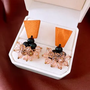 Close-up of retro wooden earrings with black beads and pink glass cluster details.