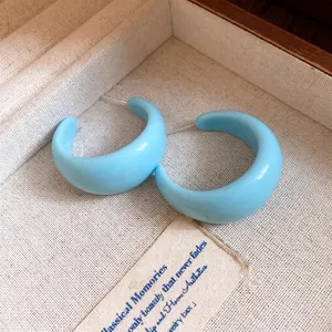 Boucles d'oreilles créoles en résine bleu clair en forme de C dans un écrin à bijoux en tissu