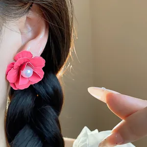 Detail view of elegant red spray-painted flower earring with pearl center worn on ear