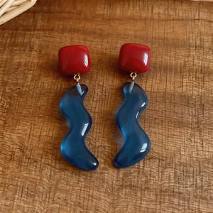 Dettaglio degli orecchini in resina a forma quadrata rossa e ondulata blu con ago in argento.