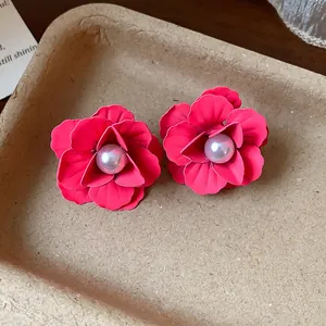 Close-up of elegant red flower earrings with pearl centers on a textured tray