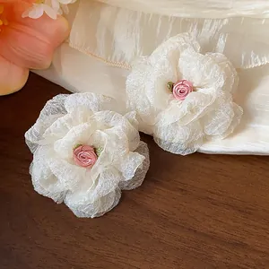 Detail of sweet chiffon flower stud earrings with a small pink rose center on wood background.
