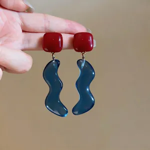 Primo piano di eleganti orecchini in resina a forma quadrata rossa e ondulata blu a mano