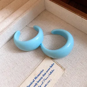 Vue détaillée de boucles d'oreilles en résine bleue en forme de C dans un écrin à bijoux