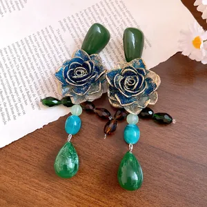 Detail view of vintage resin rose earrings with green teardrop pendants on a book.