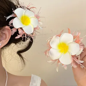 Dettaglio di un fermaglio per capelli con fiore di plumeria e piume rosa su modella asiatica.