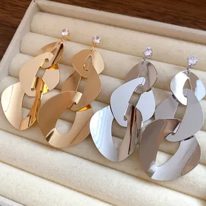 Close-up of geometric polished drop earrings with zircon studs in gold and silver
