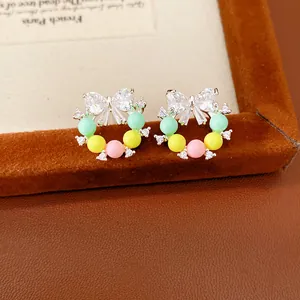 Primo piano dettagliato di orecchini a fiocco con perle in resina colorate e zirconi.