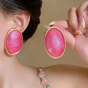 Close-up of elegant large pink resin oval stud earrings with gold frames on model's ear