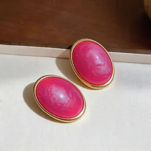 Detailed macro view of pink marble-patterned resin oval stud earrings in a gold frame