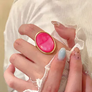 Macro view of a gold-toned ring featuring a large oval hot pink resin stone on finger.