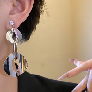 Detail view of geometric shiny silver tassel earrings with zircon stud worn on ear
