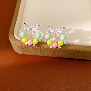 Primo piano di orecchini a forma di fiocco con zirconi e perle di resina colorate