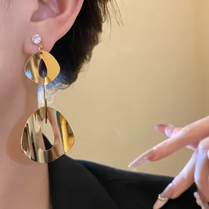 Detailed view of gold geometric drop earrings with zircon studs worn by a model