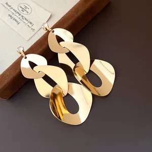 Close-up of gold geometric chain earrings with clear zircon studs on a dark background