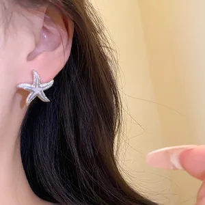 Primer plano de un delicato pendiente de estrella de mar con esmalte blanco en la oreja