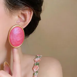 Detail view of a large pink marbled resin oval stud earring with elegant gold frame