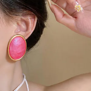Detailed close-up of pink marbled resin oval stud earrings with gold rim worn by a model