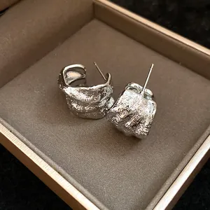 Close-up of silver-tone C-shaped earrings with unique wrinkled texture inside a box.