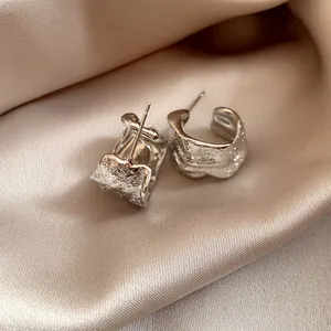 Detail shot of silver C-shaped earrings featuring a unique wrinkled lava texture