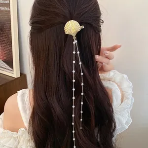 Elegant gold shell hair clip with long pearl tassels on wavy brown hair