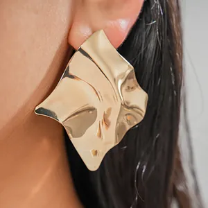 Close-up of large irregular geometric gold earring showing high-shine metal texture.