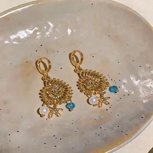 Dettaglio di orecchini dorati con ciondoli a conchiglia, perla e stella marina su ceramica