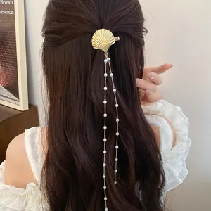 Elegant gold shell hair clip featuring long white pearl tassels worn on brown hair