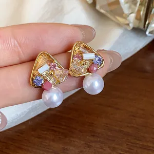Close-up of elegant triangle stud earrings with colored crystals and white pearls