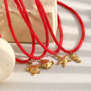 Detailopname van rode glasparelkettingen met gouden zeedierhangers op stenen decor