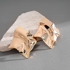 Macro detail of irregular geometric gold stud earrings with a glossy hammered texture