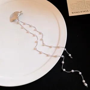 Detail of a silver shell hair clip featuring long elegant double pearl chain tassels