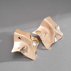 Close-up detail of irregular gold geometric stud earrings with high-shine metallic finish.
