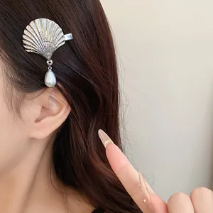 Macro view of a silver shell hair clip with a dangling white pearl teardrop pendant