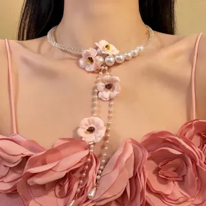 Détail élégant d'un collier ras du cou en perles avec fleurs roses et pompons romantiques