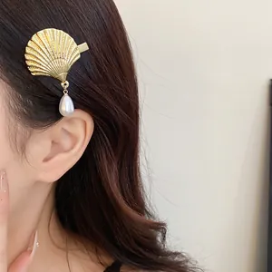 Close-up of a gold shell hair clip with a dangling pearl on dark hair, elegant detail.