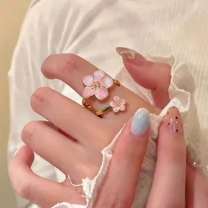 Elegante anello d'oro regolabile con due dolci fiori in smalto rosa su una mano femminile.