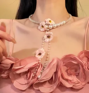 Détail d'un collier de perles avec des fleurs roses et des glands porté par un mannequin.